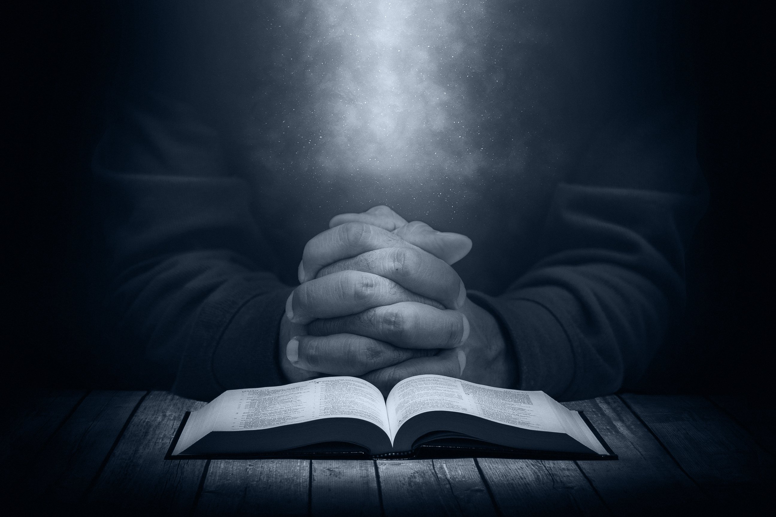 Man praying on a wooden table with an open Bible